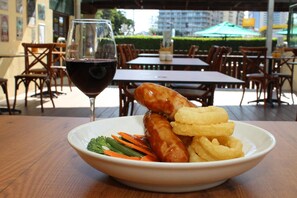 A bowl of food with sausages and onion rings on a table, with a glass of red wine beside it. - Darcy Arms Motel (Surfers Paradise)