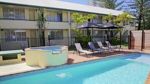 A swimming pool with lounge chairs and a hot tub, surrounded by a fence and a building with balconies. - Darcy Arms Motel (Surfers Paradise)