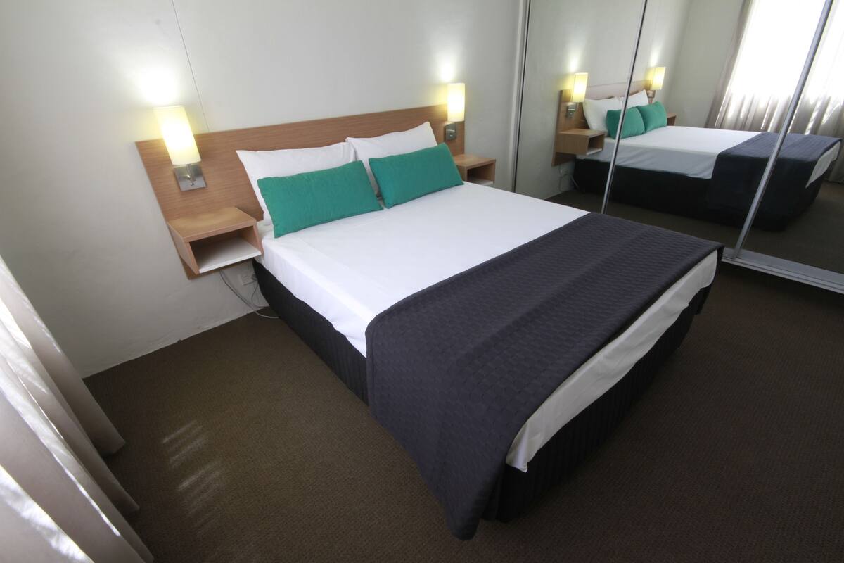 Una camera d'albergo con un letto grande, due comodini con lampade, uno specchio e un pavimento rivestito di moquette.