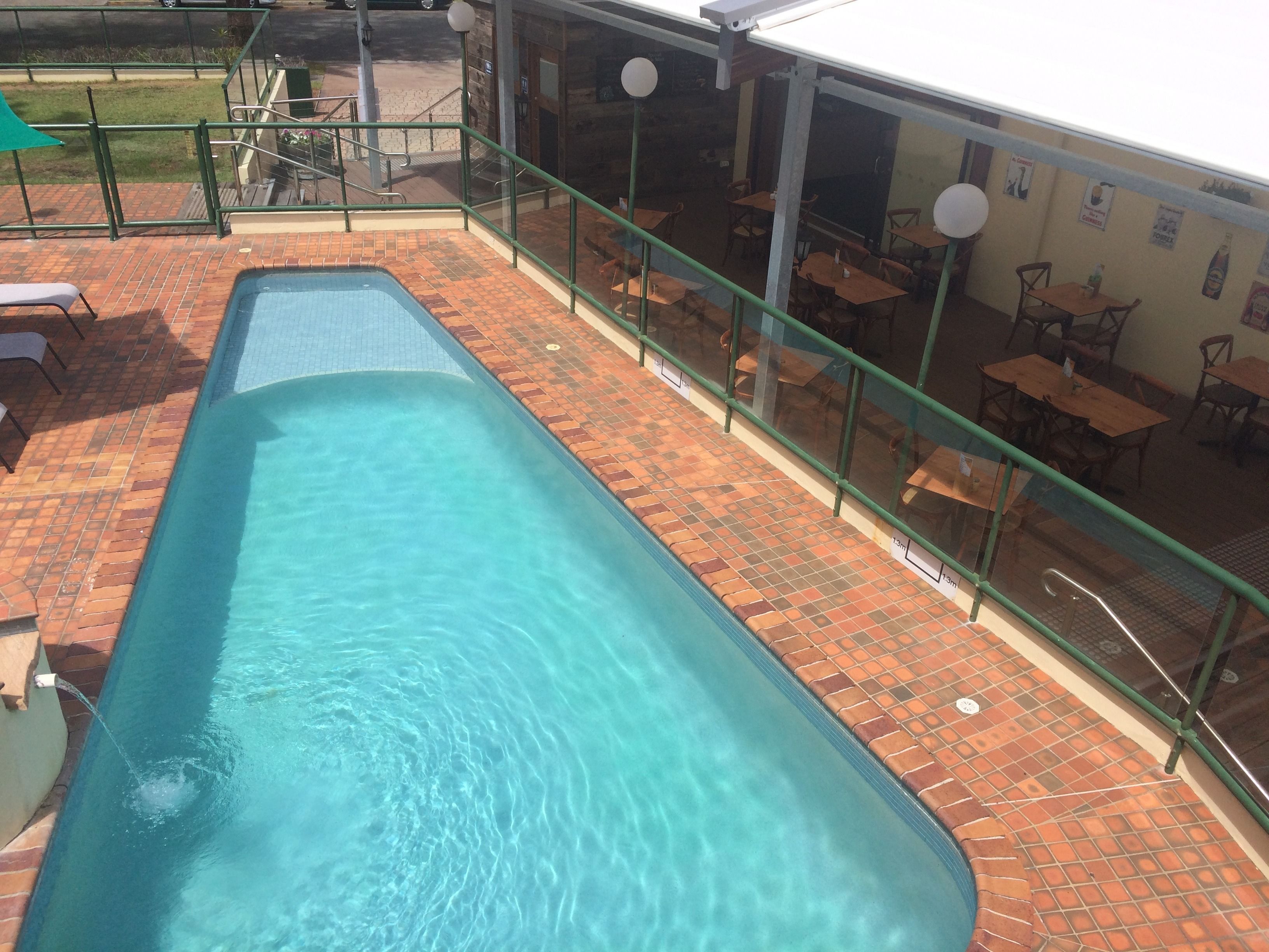 Una piscina rettangolare con acqua cristallina, circondata da un patio in mattoni e una ringhiera in vetro.