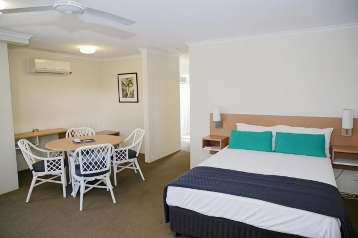 A hotel room with a bed, a desk with chairs, a ceiling fan, and a nightstand.