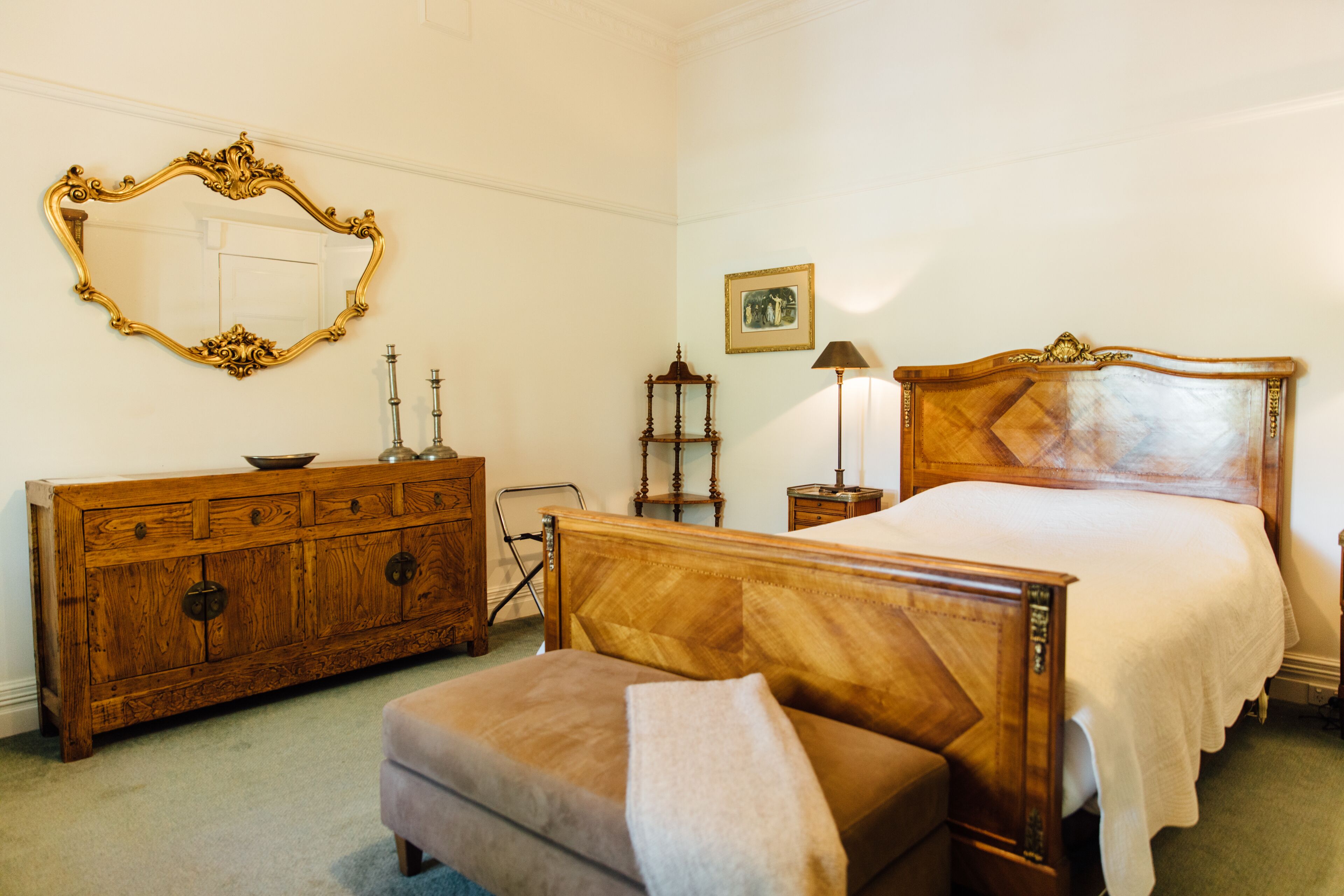 A bedroom with a wooden bed, a wooden dresser, a mirror, and a bedside table with a lamp.