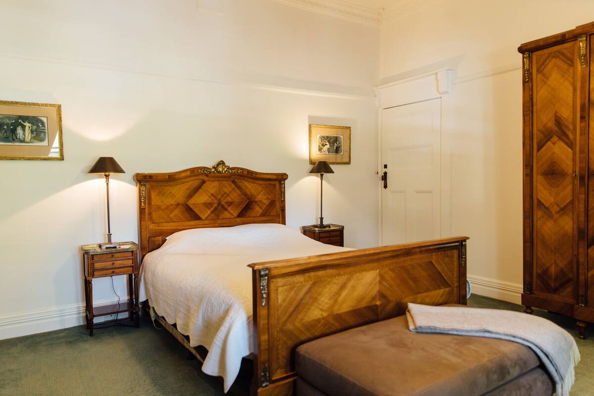 A bedroom with a wooden bed, two bedside tables, a nightstand, a wardrobe, and two wall-mounted lamps.