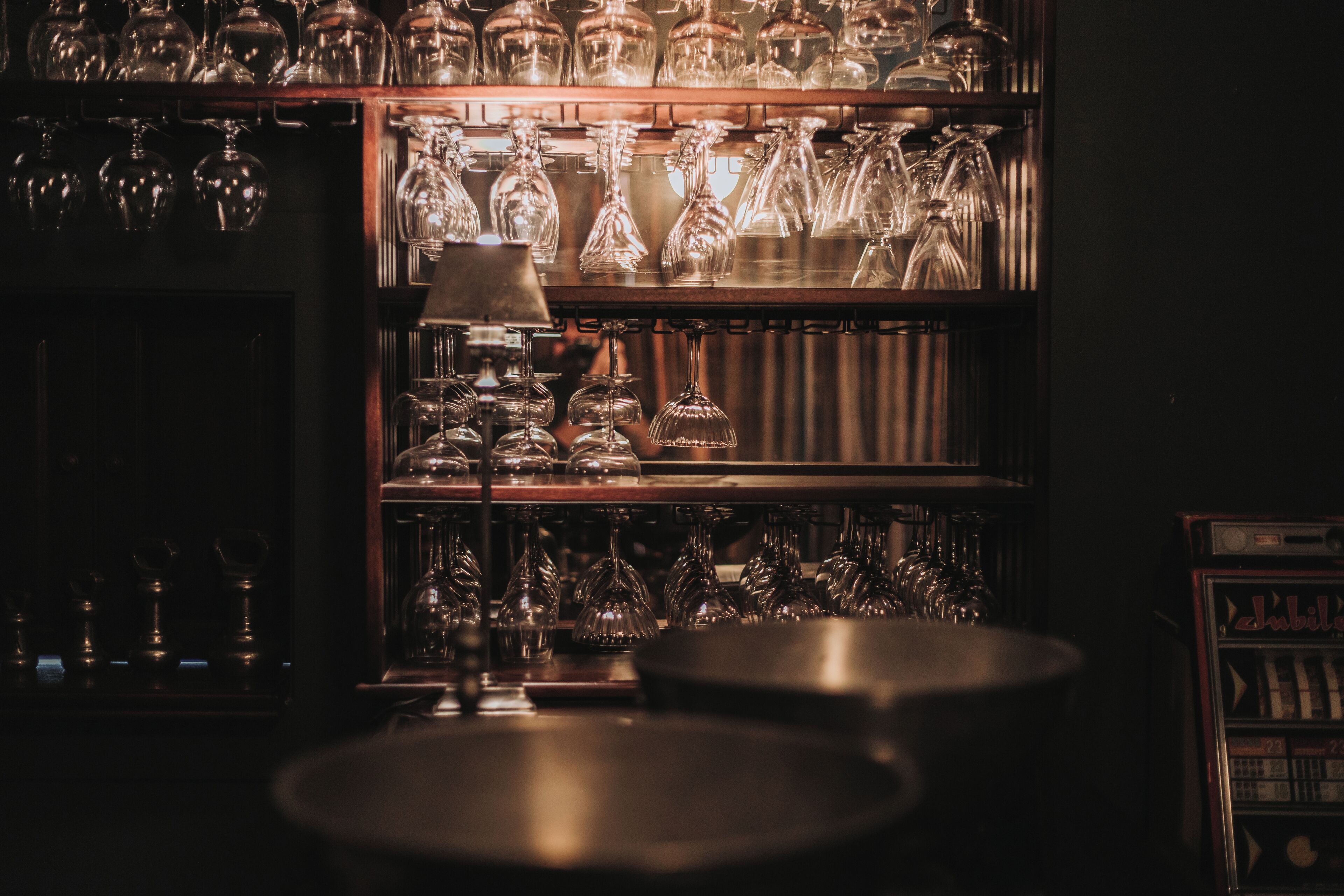 A dimly lit bar area with shelves of glassware and a vintage jukebox.