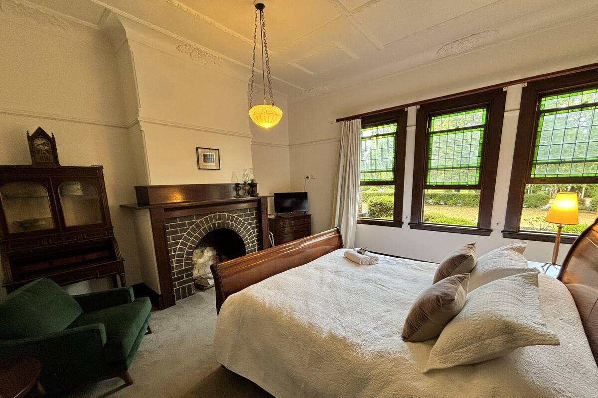 A bedroom with a large bed, a fireplace, a green armchair, and a television.