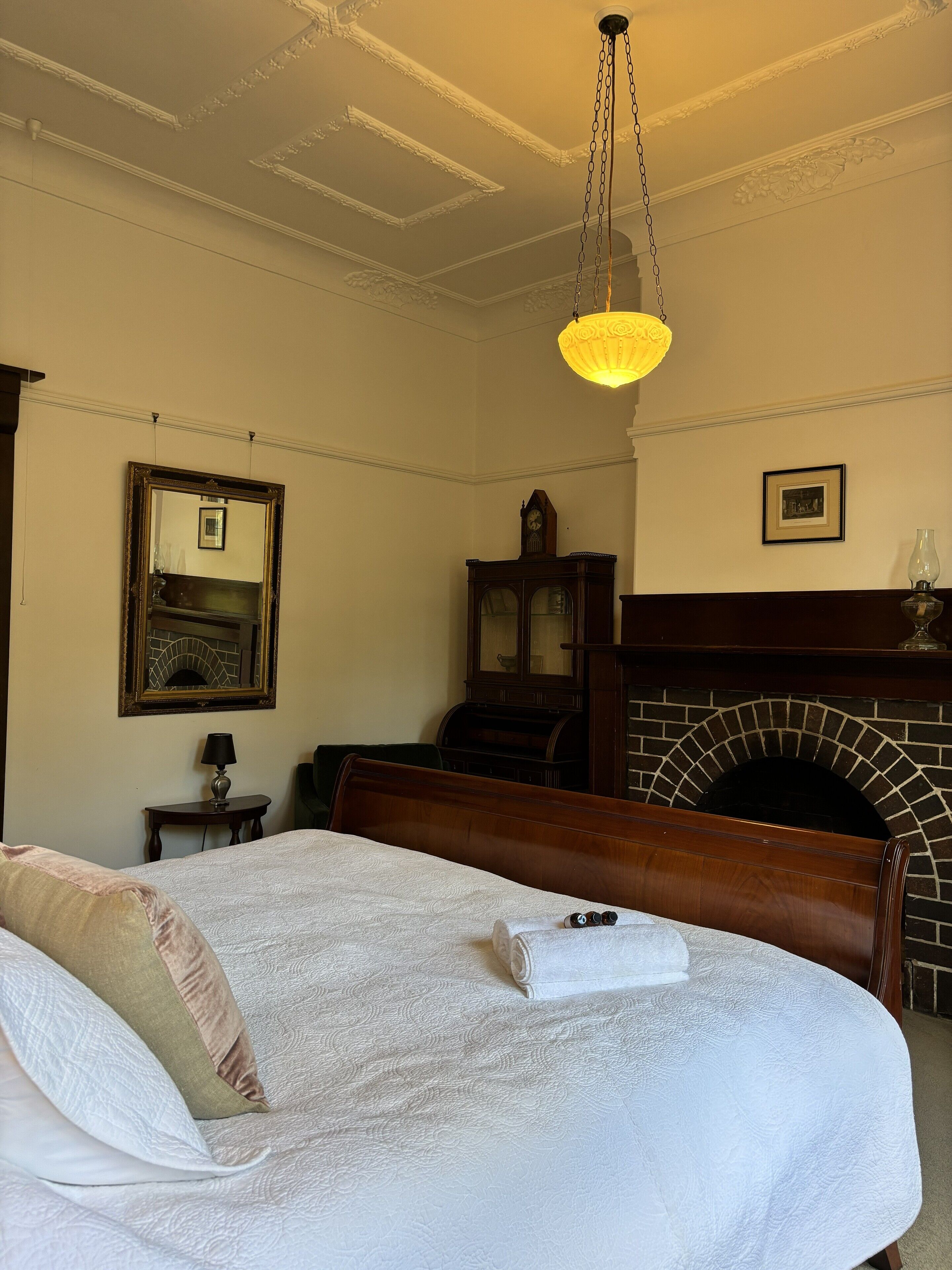 Ett hotellrum med en stor säng, en sänggavel i trä, en öppen spis, en spegel och en kristallkrona.