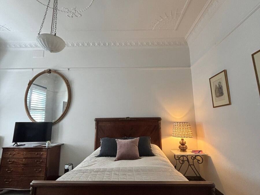 Un dormitorio con una cama de madera, un espejo redondo, un aparador, una lámpara y una lámpara del techo.