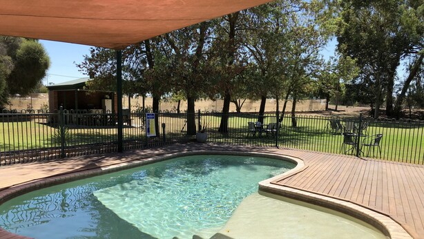 A swimming pool with a wooden deck and a fenced area with chairs. - Bullanginya Lodge (Barooga)