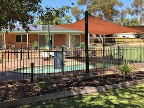 A fenced outdoor area with a pool, a shaded seating area, and a building with a green roof. - Bullanginya Lodge (Barooga)