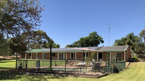 A two-story house with a green roof, solar panels, and a fenced patio area. - Bullanginya Lodge (Barooga)