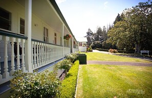 A white building with a porch and hanging flower baskets. - Okoroire Hot Springs Hotel (Tapapa)