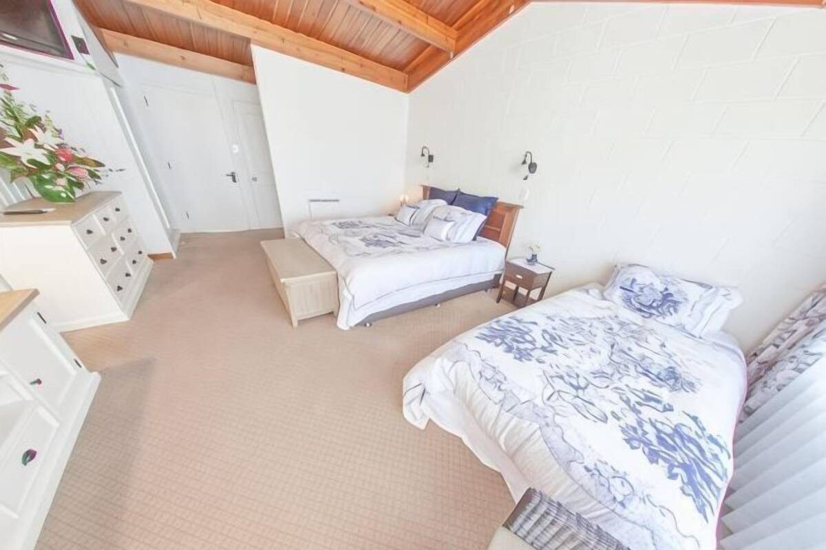 A bedroom with two beds, a dresser, a bench, and a small table.
