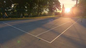 Una cancha de tenis al aire libre con una red, rodeada de árboles y una valla.