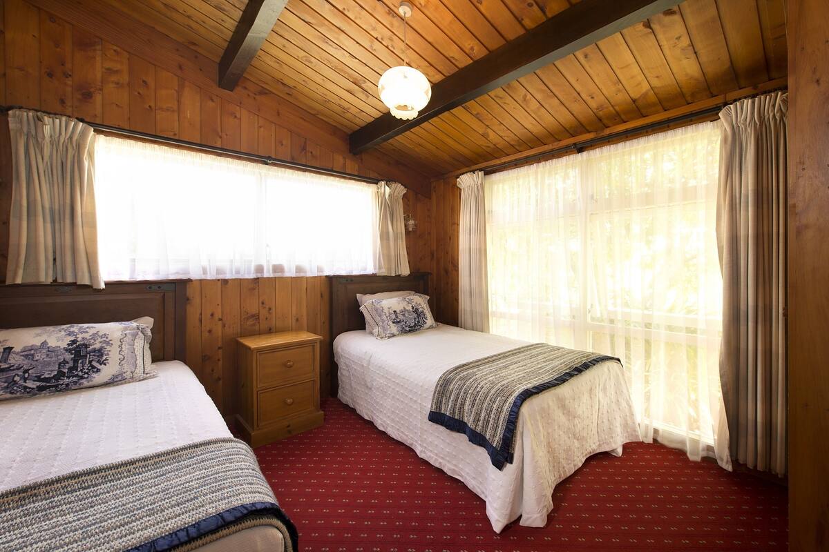 A room with two beds, wooden walls, a red carpet, and a wooden ceiling.
