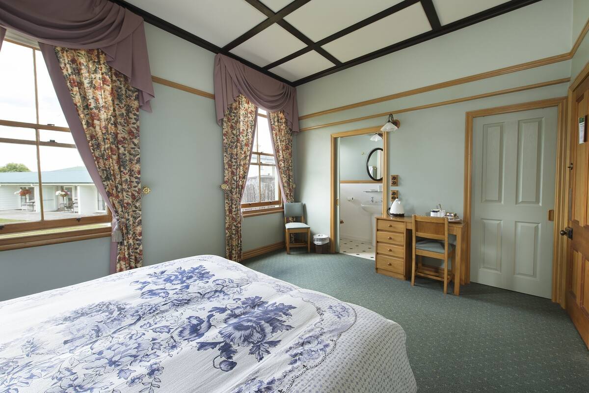 A bedroom with a bed, a desk, a chair, a mirror, and a door.