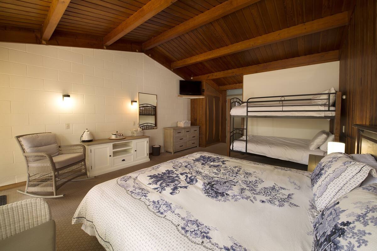 A bedroom with a bunk bed, a rocking chair, a desk with a chair, and a television on the wall.