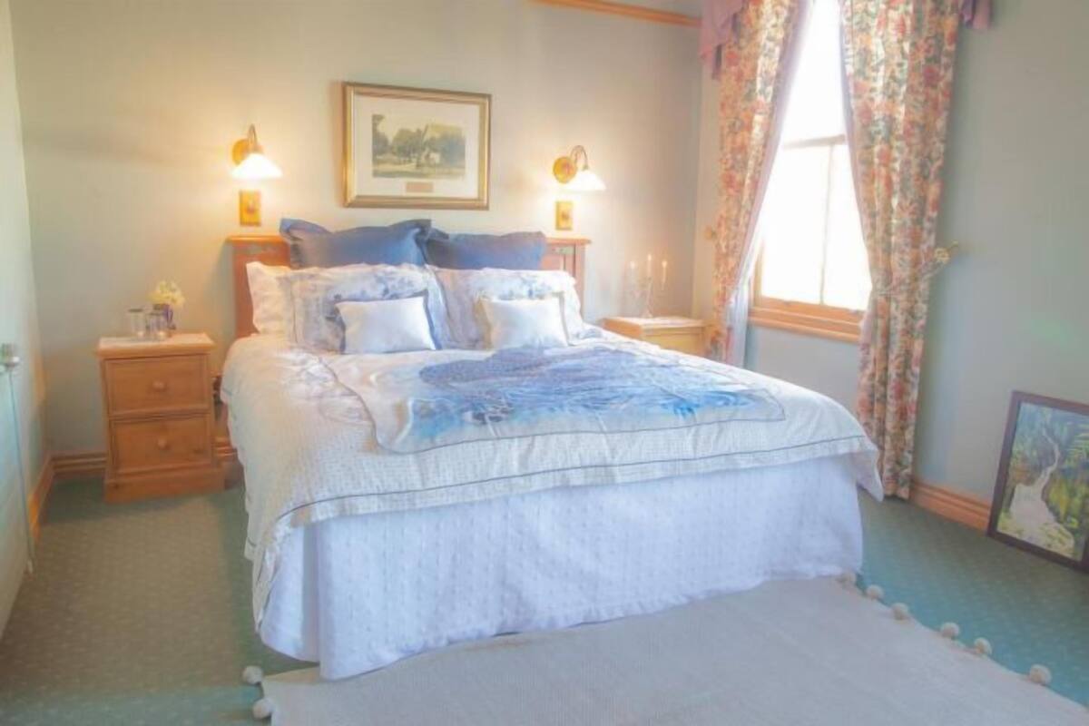 A bedroom with a bed, two bedside tables, a nightstand, a window with curtains, and a framed picture on the wall.
