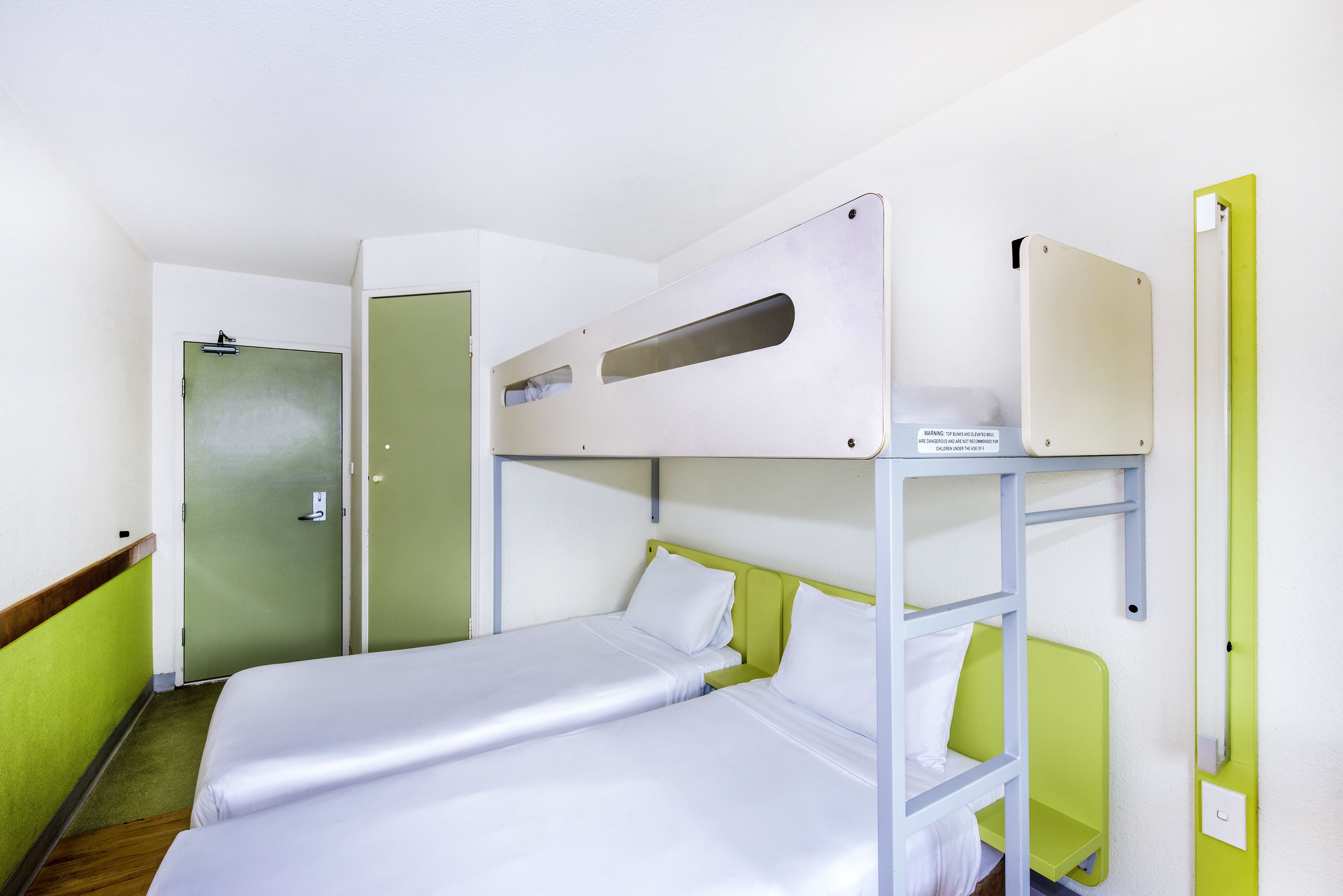 A bunk bed room with a green wall, a door, and a shelf with a box.