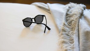 A pair of black-framed glasses on a white surface with a textured grey blanket beside them. - Ibis Budget Newcastle (Wallsend)