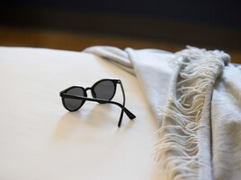 A pair of black-framed glasses on a white surface with a textured grey blanket beside them.