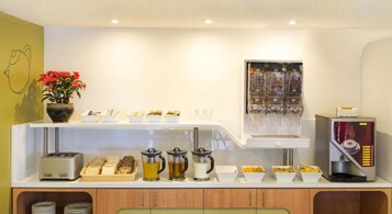 A breakfast bar with various food items, a coffee machine, and a beverage dispenser.