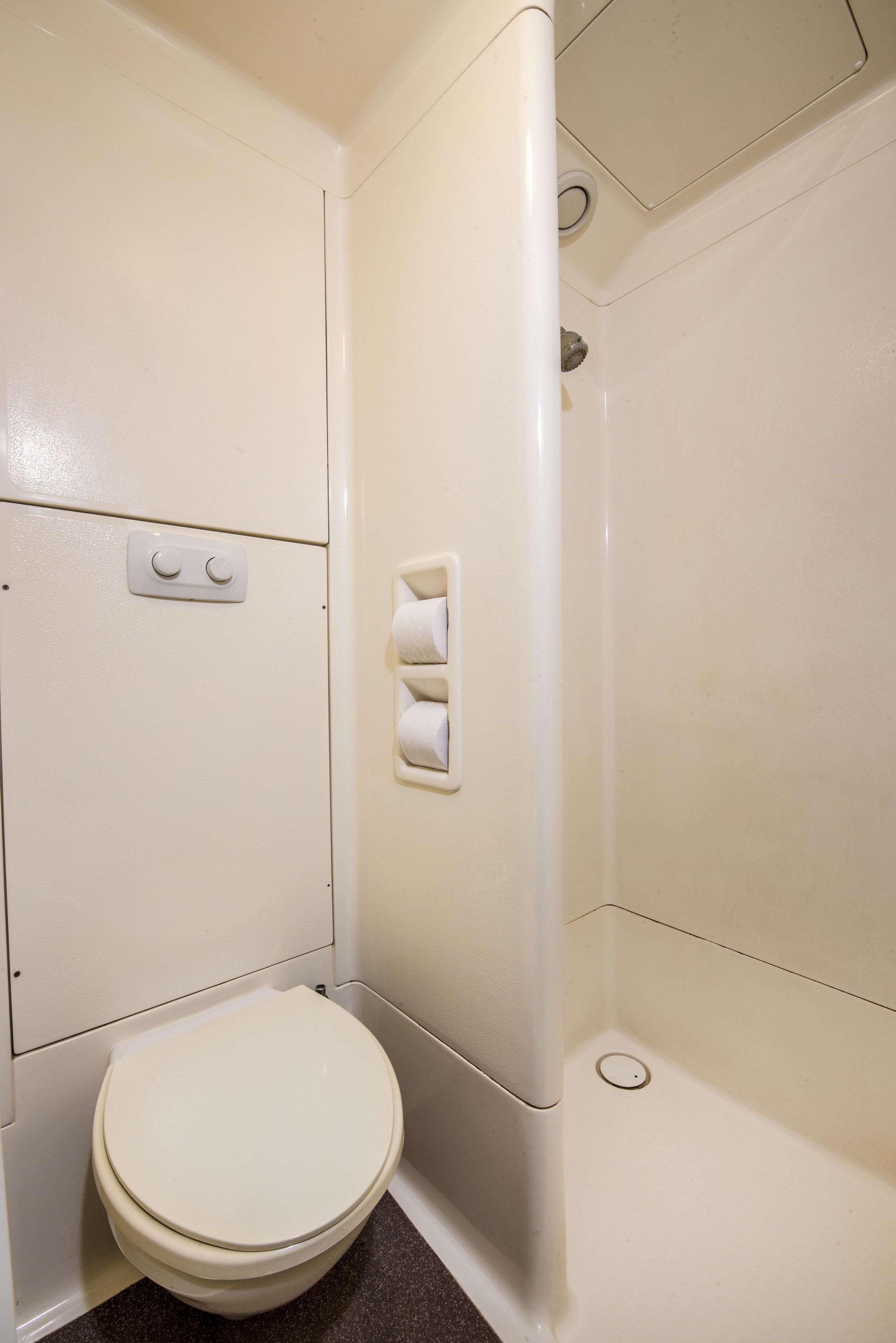 A small, white bathroom with a toilet, a shower stall, and a wall-mounted toilet paper holder.