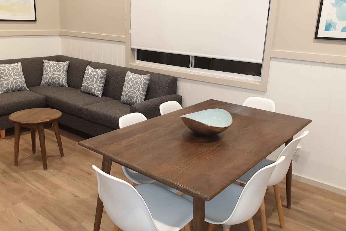 A modern living room with a sectional sofa, a wooden dining table, and white chairs.