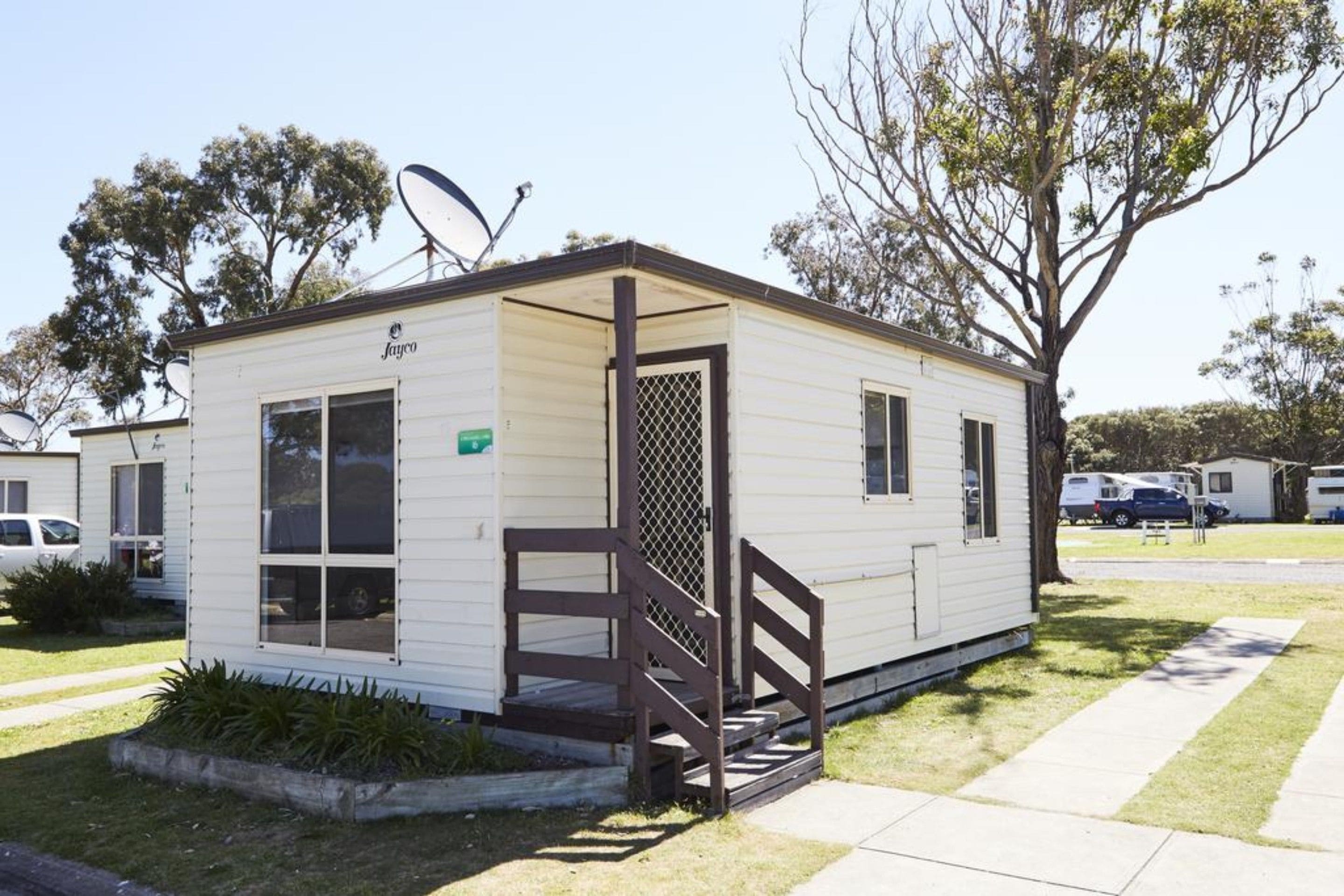 A small, single-story mobile home with a brown front porch and a satellite dish.