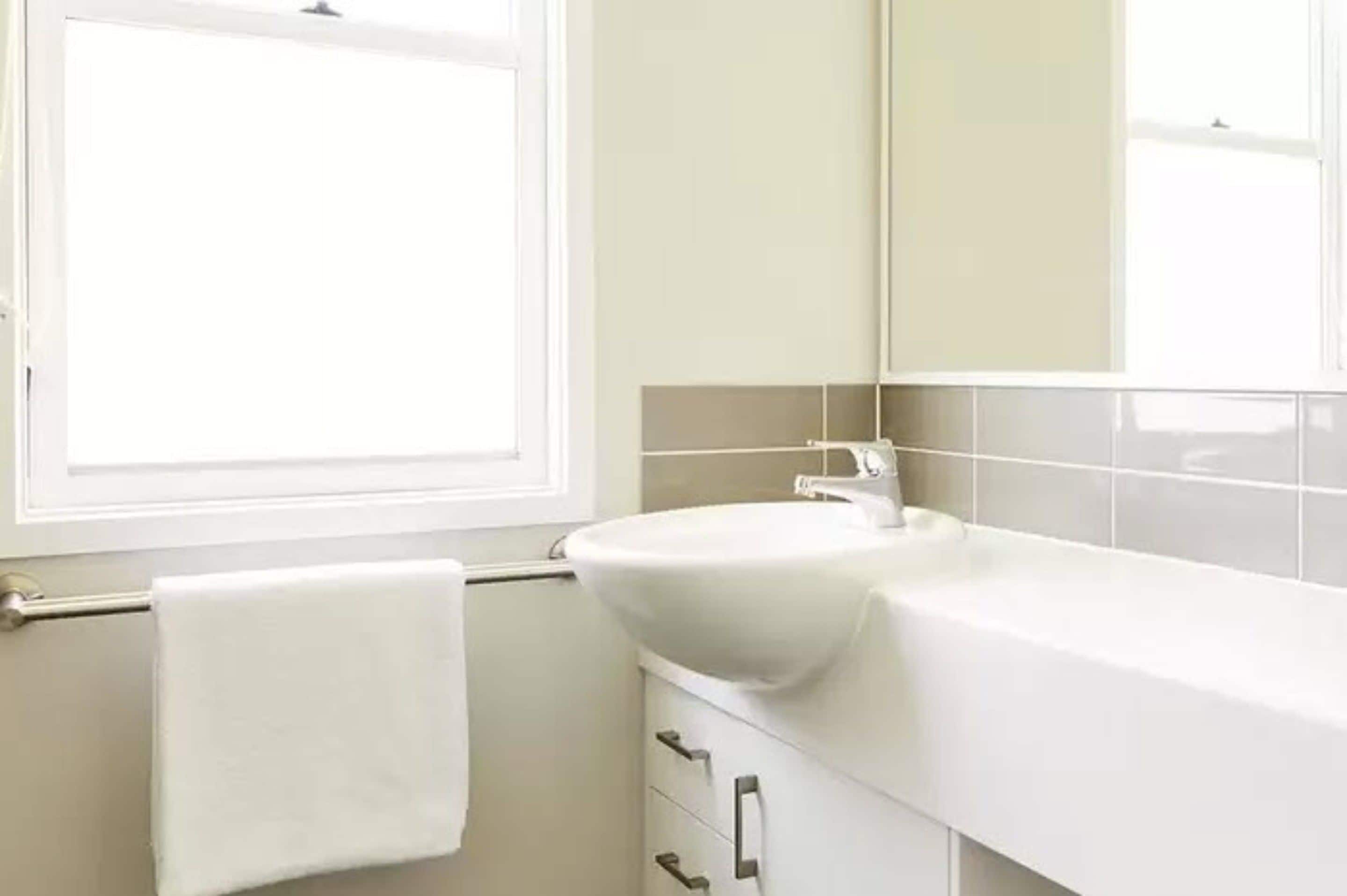 A bathroom with a white sink, a mirror, and a window.