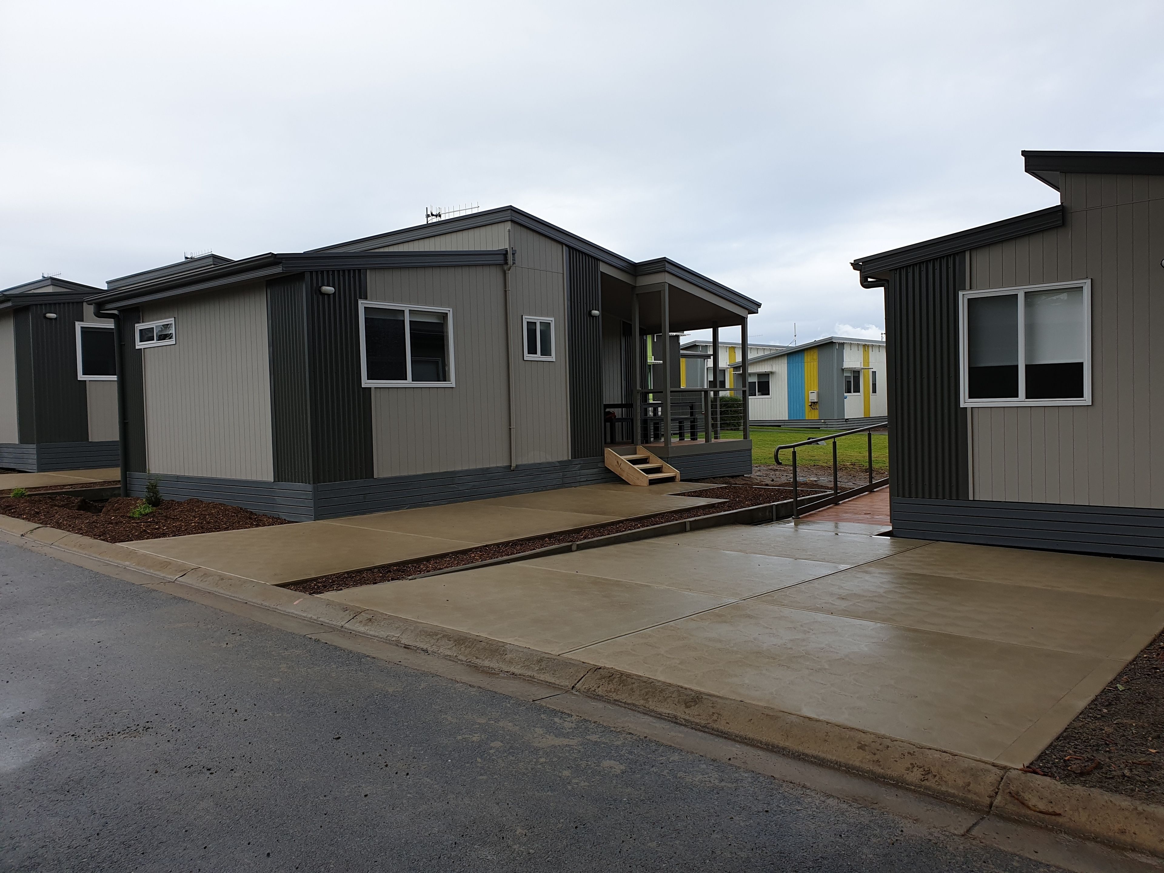 A row of modern, single-story mobile homes with a covered porch and a small set of stairs leading to the entrance.