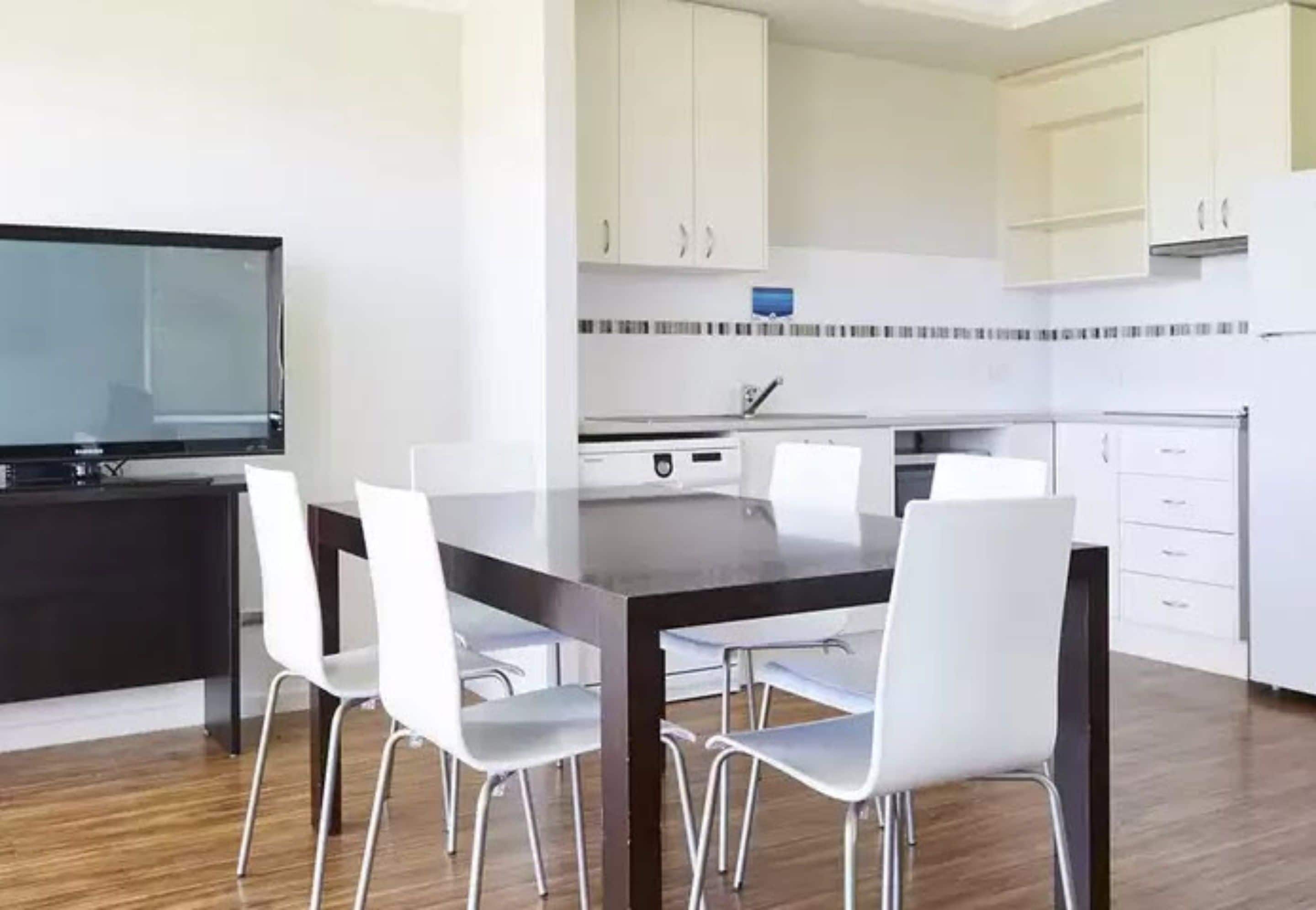 A modern kitchen with white cabinets, a black countertop, and a dining area with a dark table and white chairs.