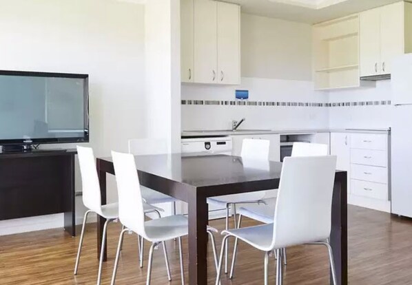 A modern kitchen with white cabinets, a black countertop, and a dining area with a dark table and white chairs.