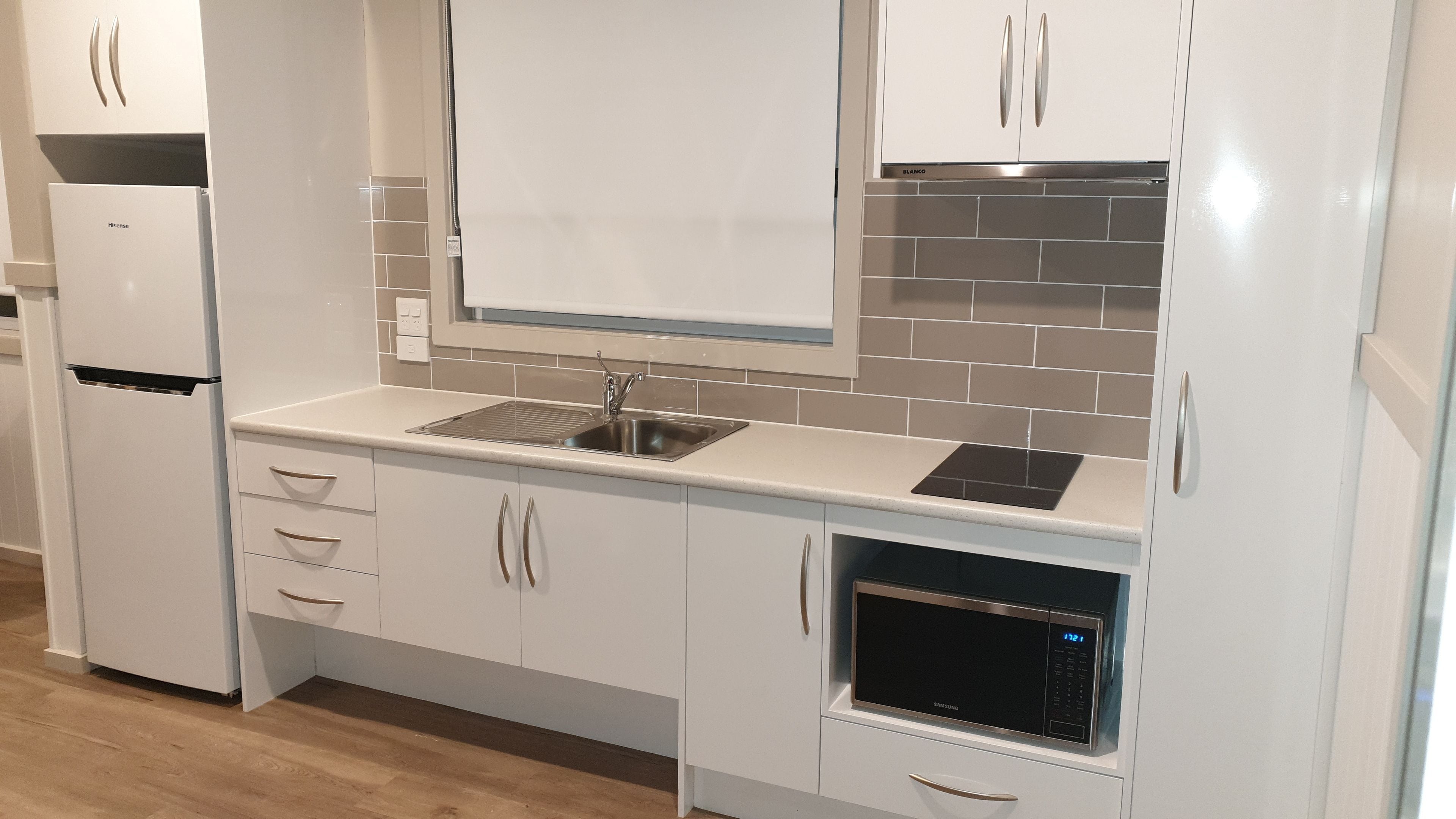 A modern kitchen with white cabinetry, a built-in sink, a microwave, and a refrigerator.