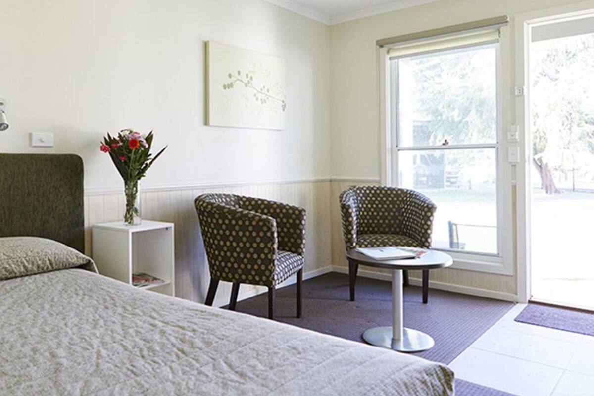 A hotel room with a bed, two armchairs, a small table, a vase with flowers, and a window with a view.