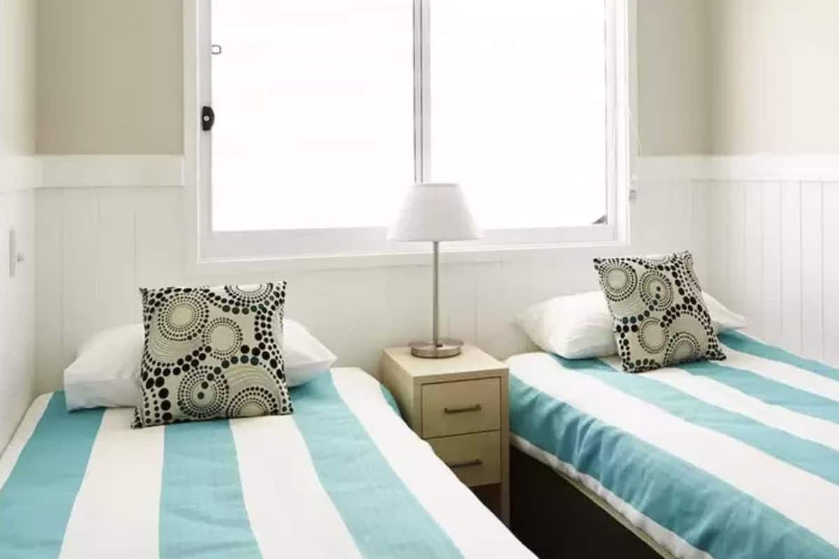 A hotel room with two beds, each with a striped bedspread, a bedside table with a lamp, and patterned pillows.