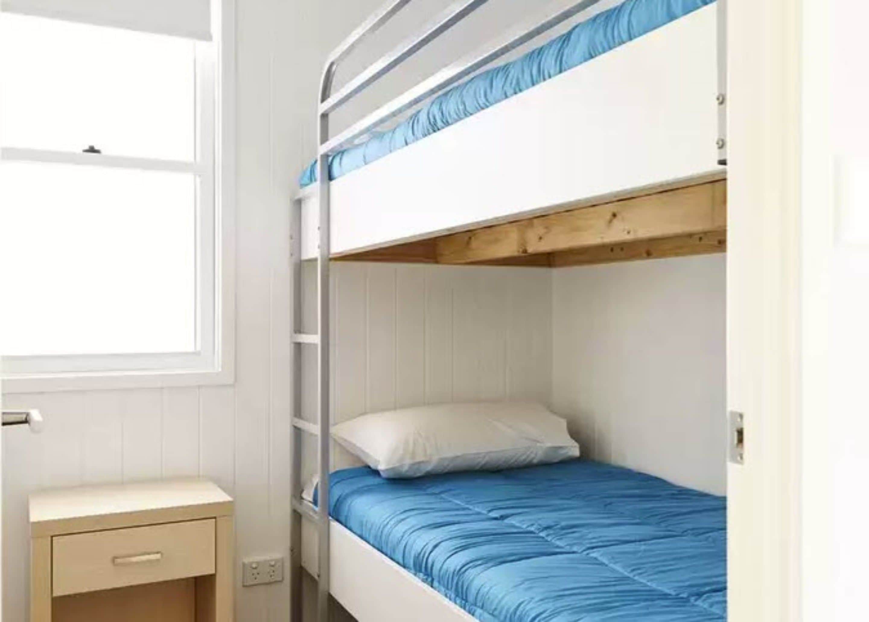 Un lit superposé avec une tête de lit en bois, un lit simple en dessous et une petite table de chevet avec un tiroir.