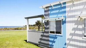 Una casa a un piano con facciata blu e bianca, un portico coperto e vista sull'oceano.