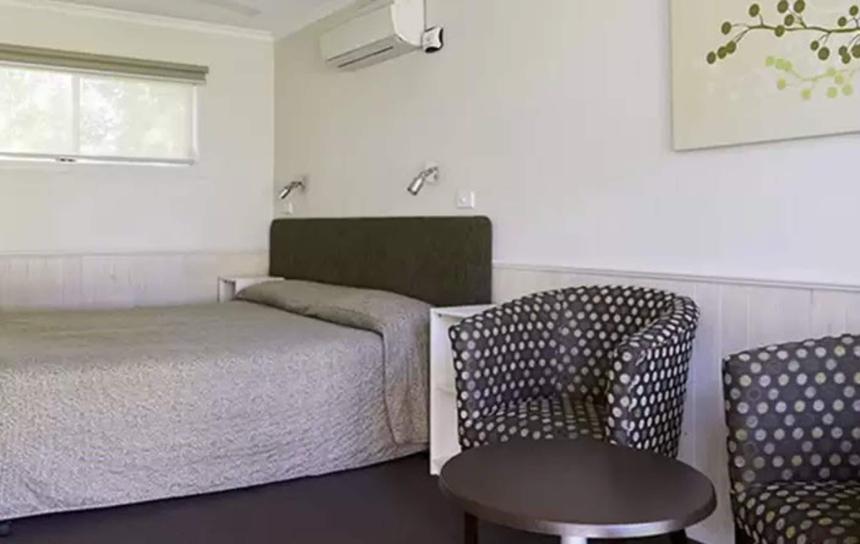 Une pièce comprenant un lit, deux fauteuils à motifs, une petite table et un climatiseur fixé au mur.