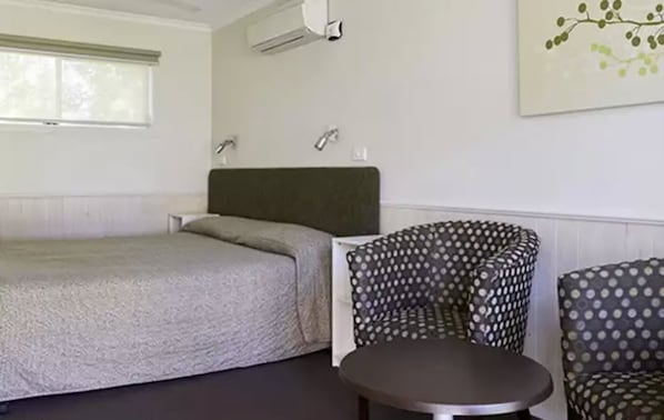 A room with a bed, two patterned chairs, a small table, and a wall-mounted air conditioning unit. - NRMA Victor Harbor Beachfront Holiday Park (Victor Harbor)