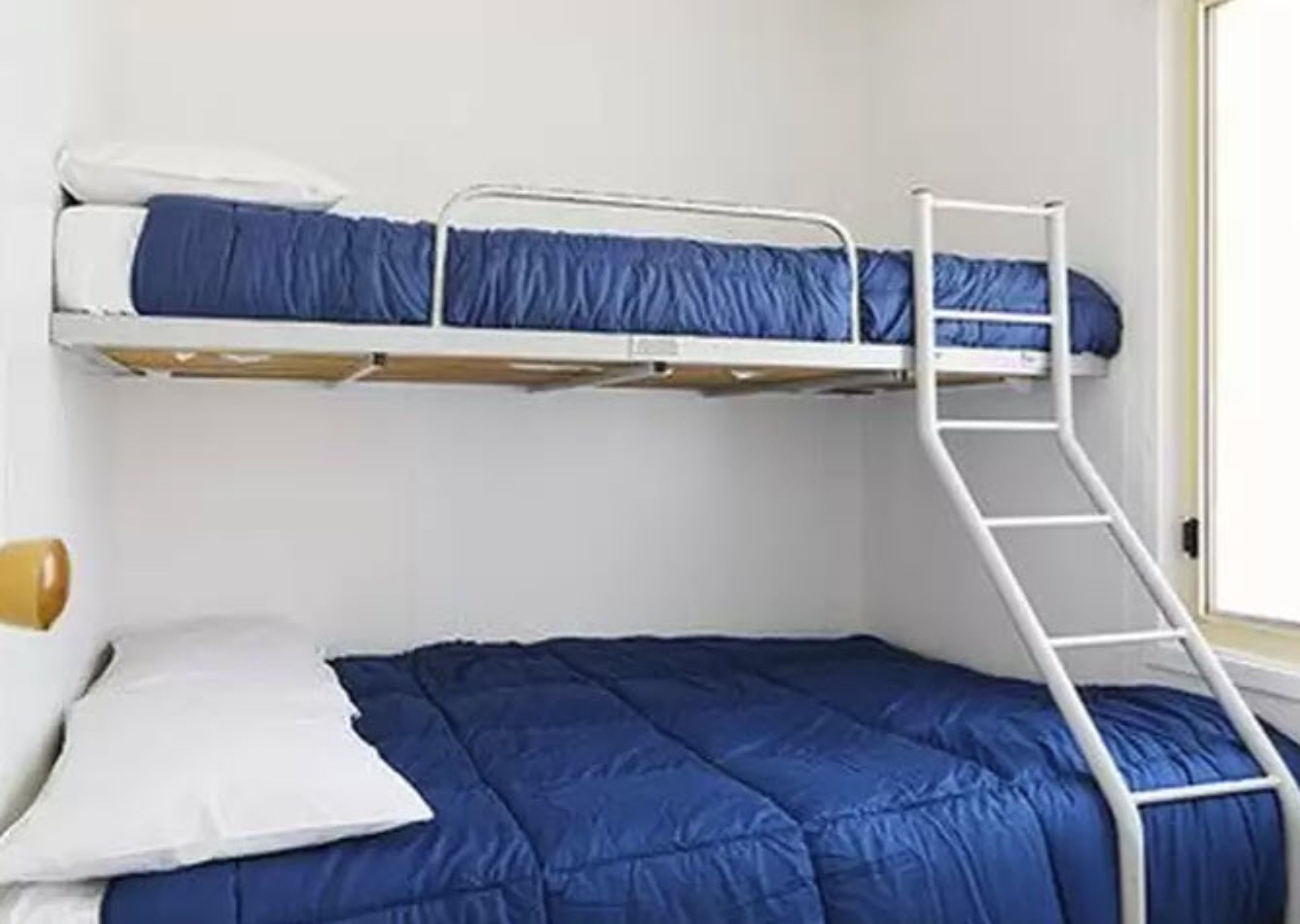 A bunk bed with a ladder, white walls, and a window.