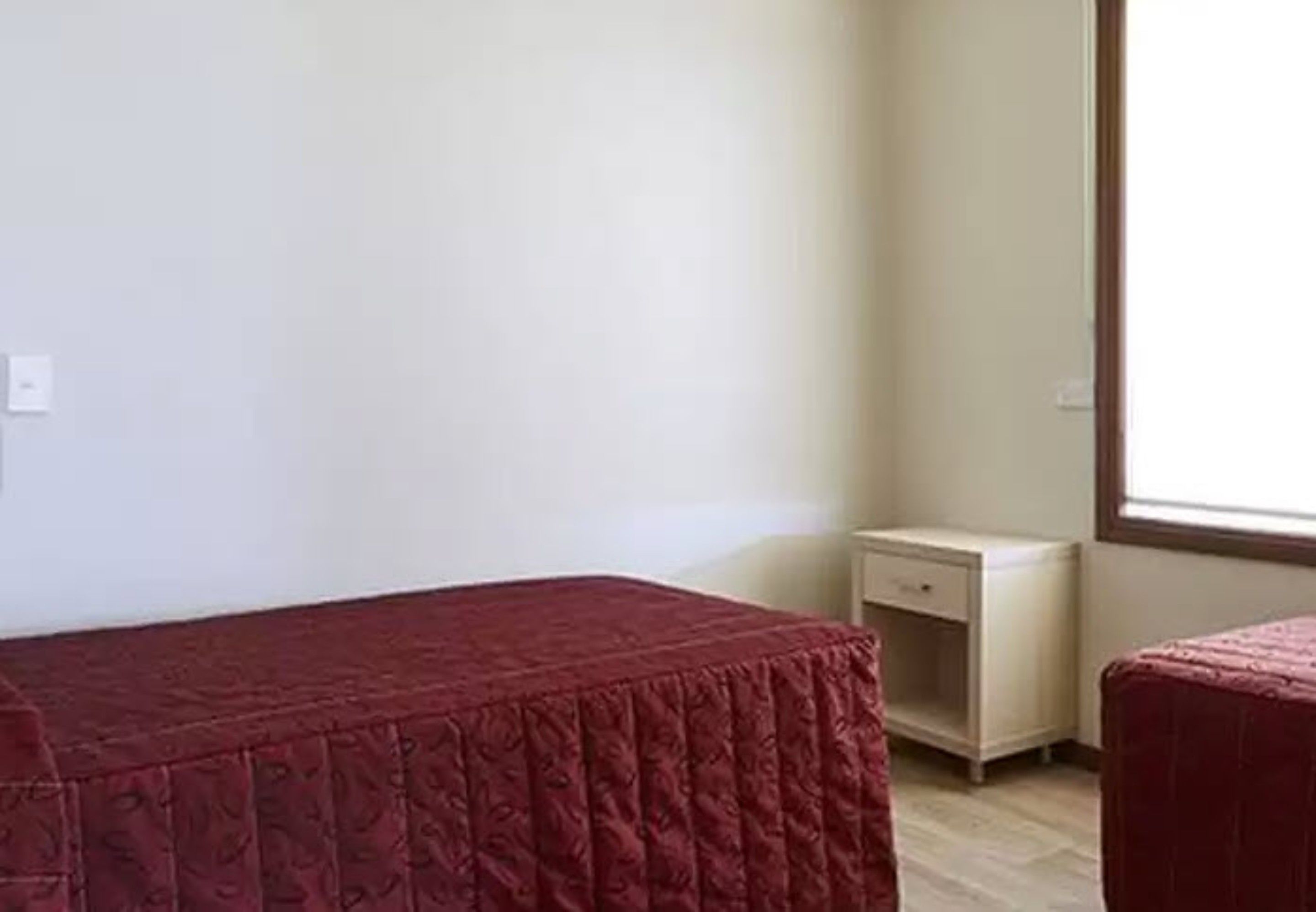 A room with a single bed, a nightstand, and a window.