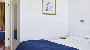 Una habitació d'hotel amb un llit, una tauleta de nit, una làmpada de paret i un quadre encimbellat a la paret.