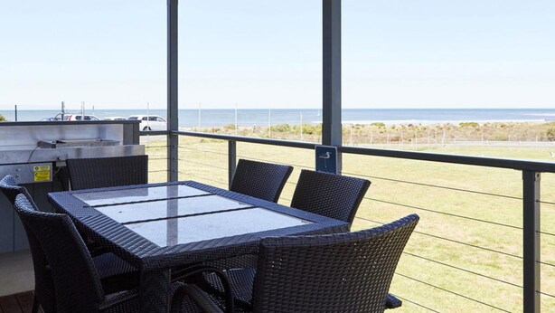 Un'area esterna coperta con tavolo e sedie, un barbecue e vista sull'oceano.