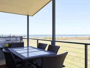 A covered outdoor area with a table and chairs, a grill, and a view of the ocean.