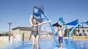 Un'area giochi con acqua dove bambini giocano, con getti d'acqua e una zona dove schizzare.
