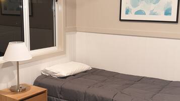 Une chambre à coucher comprenant un lit, une table de chevet avec une lampe, un ventilateur de plafond, une fenêtre et un tableau abstrait accroché au mur.