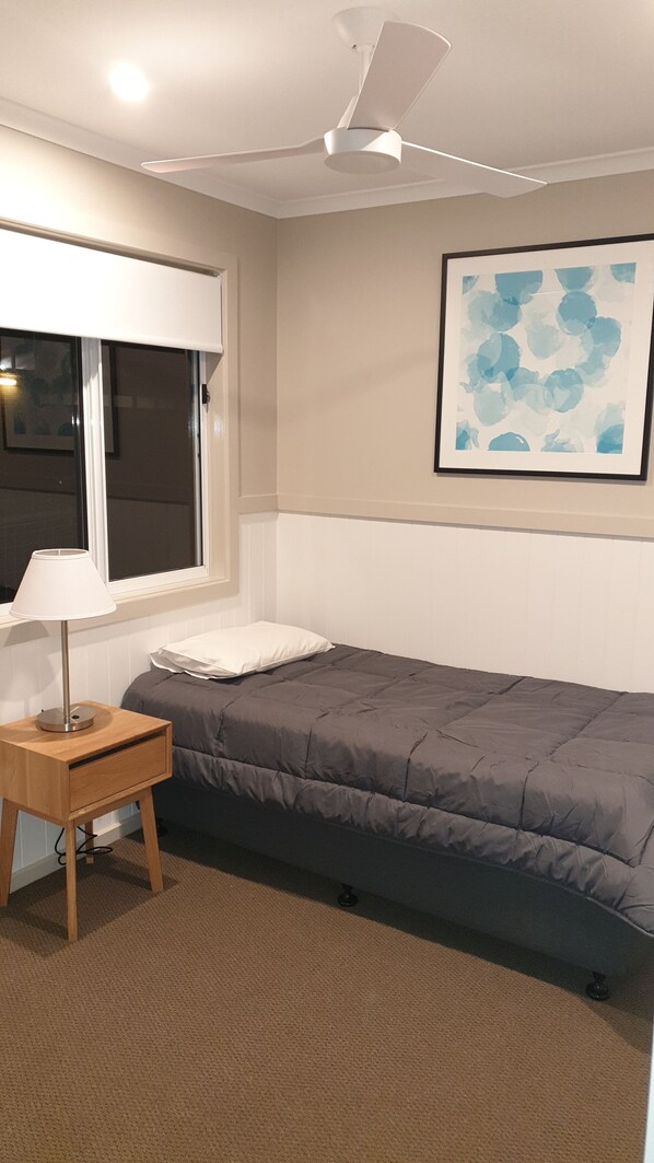 A bedroom with a bed, a bedside table with a lamp, a ceiling fan, a window, and a wall-mounted abstract painting. - NRMA Victor Harbor Beachfront Holiday Park (Victor Harbor)