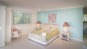 Un dormitorio con cama, dos mesitas de noche, una silla, una ventana con persianas y un adorno en la pared.