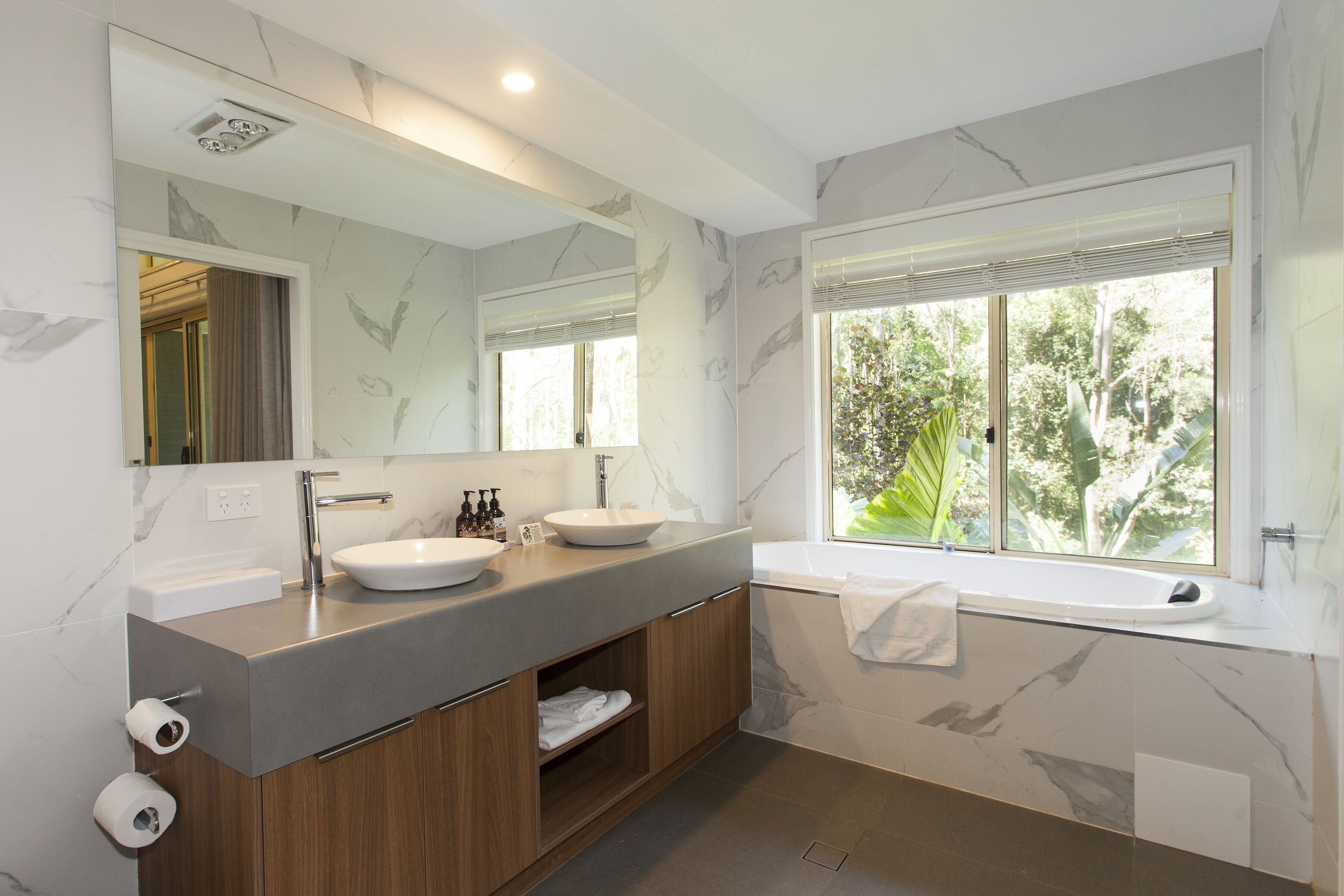 A modern bathroom with two sinks, a large mirror, and a bathtub.