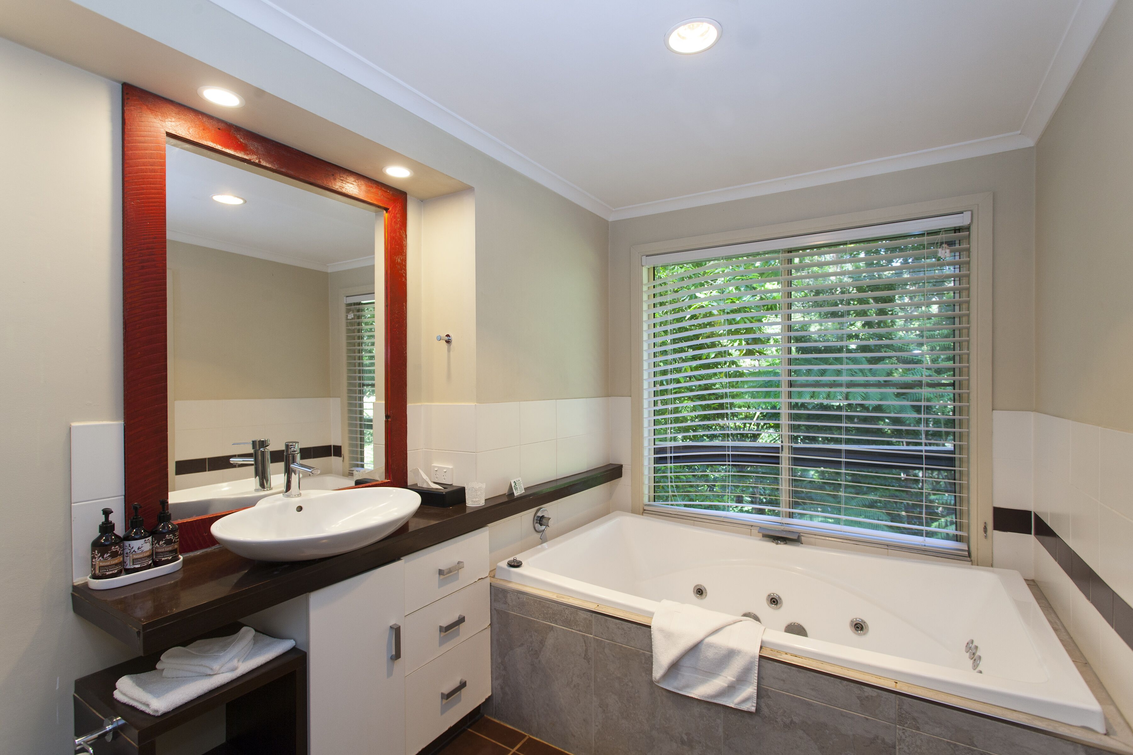 A modern bathroom with a large sink, a bathtub, and a window with blinds.